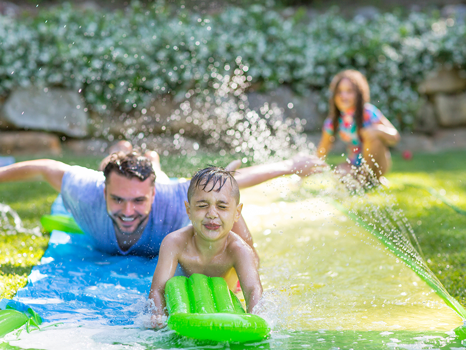 Vater spielt mit Kindern auf einer Wasserrutsche im Garten