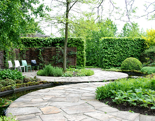 Geschwungener Gartenweg mit Gartenteich und grüner Bepflanzung am Rand