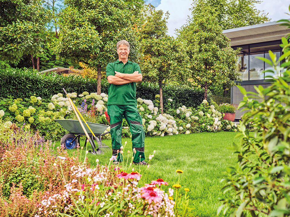 Landschaftsgärtner mit Signum steht vor dem Garten