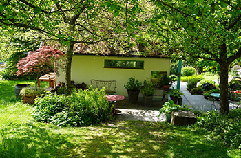 Blick in einen Garten, im Vordergrund sind Cortenstahlelemente im Hintergrund eine Sitzecke und eine Rasenfläche